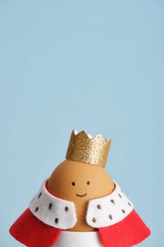 Easter egg featuring king with crown and red robe close up on blue background. Place for your text.