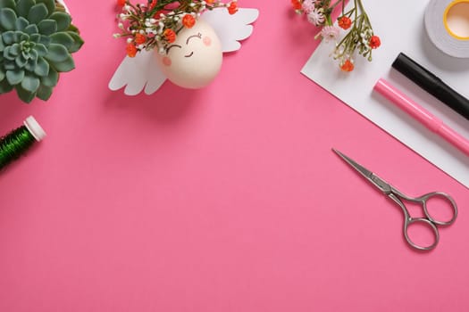 DIY egg angel with floral decorations on a pink background. Easter background. Place for your text.