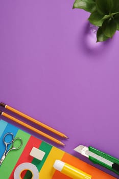 Paper craft table: scissors, knife, pencil, eraser, colored paper on purple background. Space for your text.