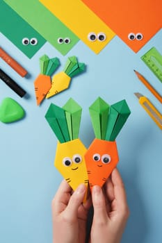 Making origami carrot. DIY project. Hands holding the finished crafts. Yellow and orange carrots with eyes and smiles.