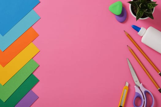 Supplies for paper art hobby: scissors, craft knife, pencil, eraser, colored paper on pink background. Space for your text. Paper crafts work table flatlay.