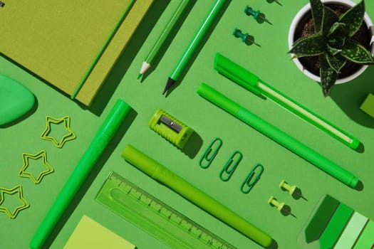 Knolling stationery composition in green theme. Spiral notebook, pens, pencil, sharpener, sticky notes, eraser, paper clips, push pins
