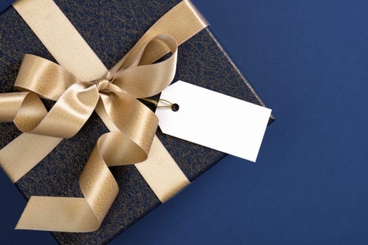 Card with dark blue gift box with gold ribbon and blank rectangular label. Space for your text