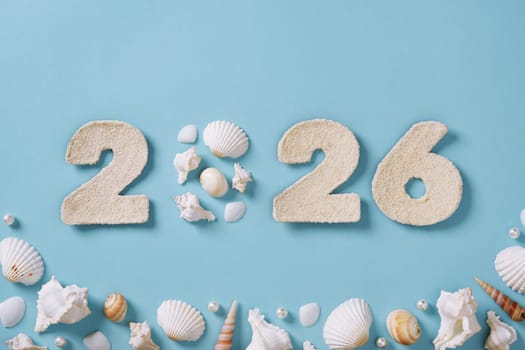 The number 2026 is crafted from fine sand and displayed against a light blue background. Surrounding the numerals are various seashells. Upcoming new year.