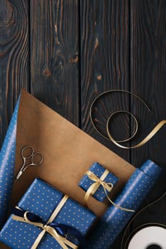 Supplies for gift wrapping. Wrapping paper, tags, and ribbon in blue and gold colors. Wooden background, space for your text.