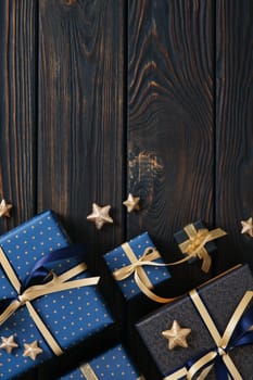 Gifts wrapped in blue paper and gold ribbons lie on a wooden background. A place for your text.