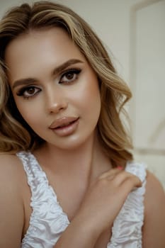 close up of happy attractive blonde in white silk lingerie in bright bedroom. smiling at camera, close up portrait. concept of face and skin care at home, bride's morning