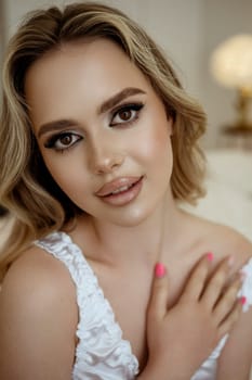 close up of happy attractive blonde woman in white silk lingerie. wavy hair, beautiful makeup. smiling at camera, close up portrait. Face and skin care concept at home, bride's morning