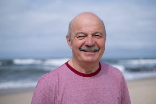 An elderly man with a mustache walking on the beach