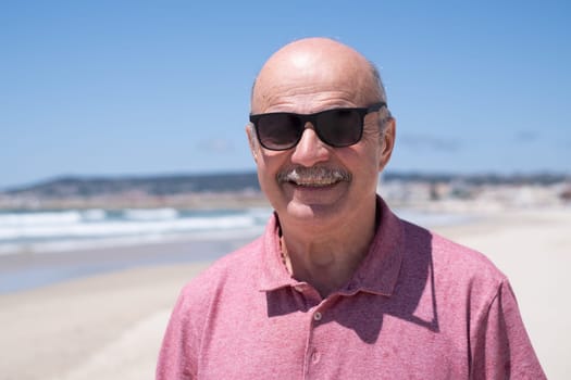 An elderly man with a mustache walking on the beach