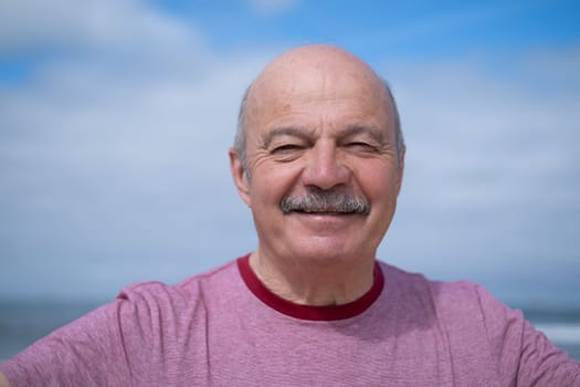 An elderly man with a mustache walking on the beach