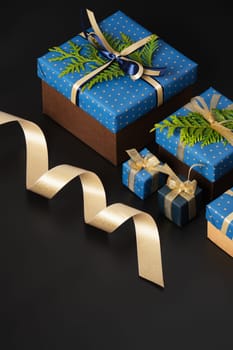 Selective focus wrapped gifts decorated with blue polka dot paper, gold ribbons and sprigs of fresh greenery on a black background. Space for your text