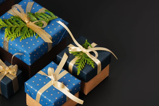 Selective focus wrapped gifts decorated with blue polka dot paper, gold ribbons and sprigs of fresh greenery on a black background. Space for your text