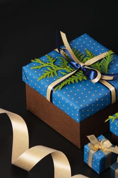 Selective focus wrapped gifts decorated with blue polka dot paper, gold ribbons and sprigs of fresh greenery on a black background. Space for your text