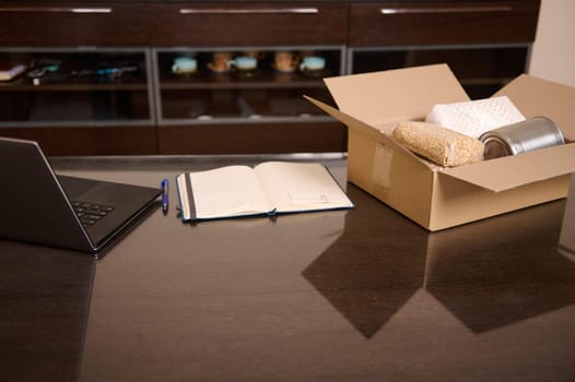 Desk setup featuring a laptop, notebook, and delivery box with items. Perfect for concepts of business, online retail, supply chain, productivity, and remote work environments.