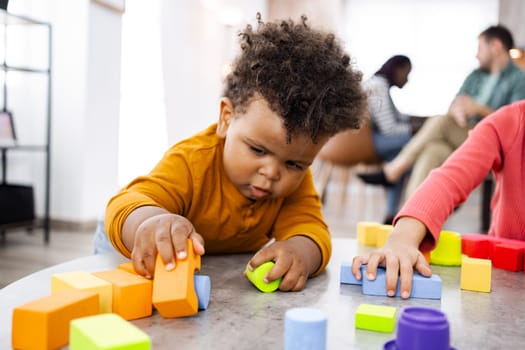 Children engage in colorful block play with family nearby.