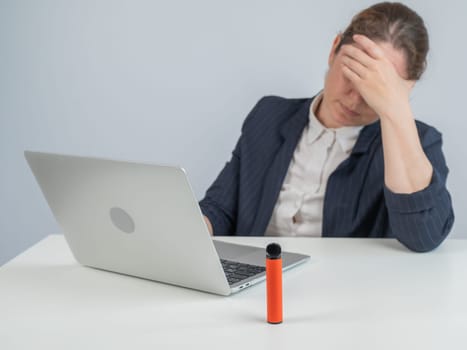 Caucasian businesswoman working on laptop. Disposable vape in foreground