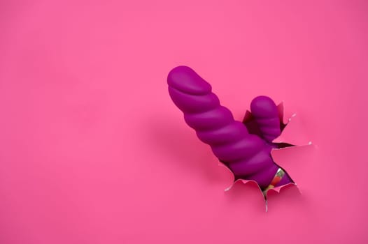 Raspberry sex toy sticks out of pink paper background. Copy space