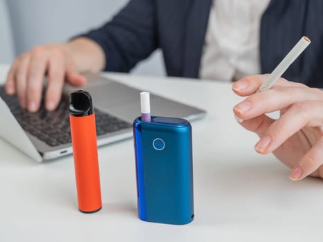 A woman demonstrates different types of cigarettes. An e-cigarette, a disposable vape, and a regular cigarette