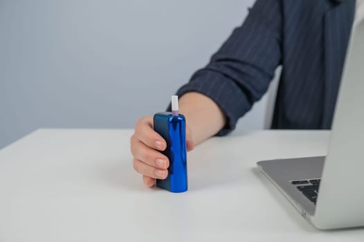 Business woman smoking an electronic cigarette while working on a laptop. Tobacco heating system