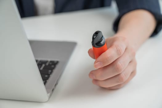 Faceless businesswoman smokes disposable vape and works on laptop