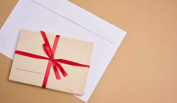 A stack of blank postcards tied with a red ribbon with a bow and an envelope lie on a beige background.