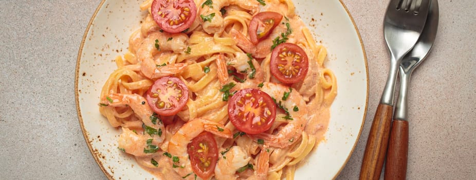 Seafood linguine pasta in creamy sauce with shrimp and cherry tomatoes, garnished with fresh parsley, served on a light warm beige background with cutlery top view