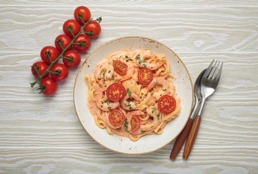 Seafood linguine pasta in creamy sauce with shrimp and cherry tomatoes, garnished with fresh parsley, served on white wooden background with cutlery top view