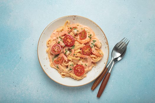 Seafood linguine pasta in creamy sauce with shrimp and cherry tomatoes, garnished with fresh parsley, served on a light blue background with cutlery top view
