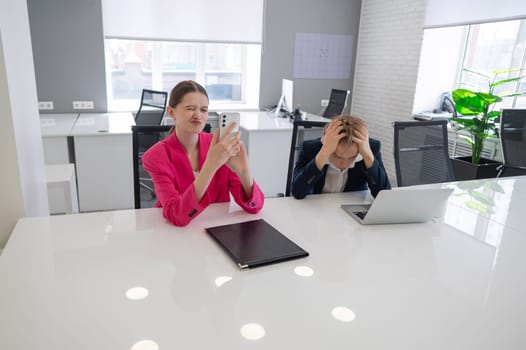 Caucasian Businesswoman Uses Smartphone While Colleague Has Problems At Work