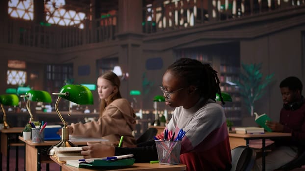 University student engrossed in texting with classmates at the library, chatting with friends instead of studying. Girl discussing with colleagues about an assignment. Camera B.