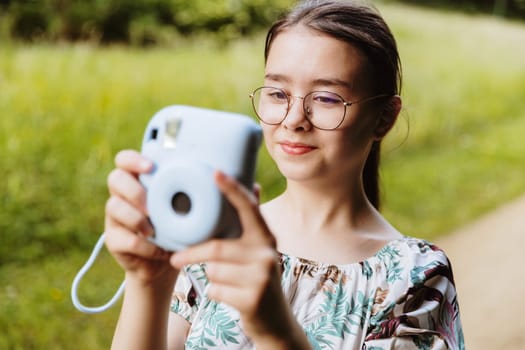 Portrait of a beautiful Caucasian girl taking pictures with a camera in a park on a spring sunset day, side view, very close-up. Happy childhood concept, children bloggers.