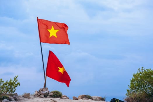 Vietnamese flag on top of mountain. Red symbol of Vietnam in nature on background of sky. Concept of victory and win