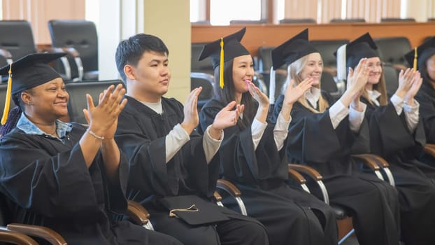 Graduates sit on a bench, listen to the speech and applaud