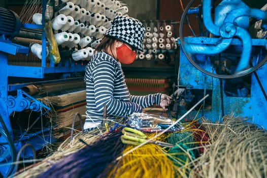 Vietnamese female weaver works on a loom in workshop at a factory producing traditional woven reed mats in Vietnam in Asia
