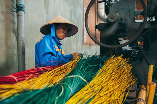 Vietnamese woman in a straw hat works at a loom in a factory for the production of woven reed mats. An Cu, Tuy An, Phu Yen province, Vietnam - April 14, 2025