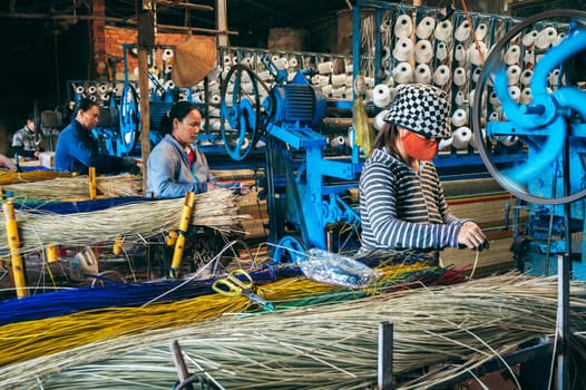 Vietnamese women weavers works at a looms weaving machines in a factory for production of woven reed mats in Vietnam in Asia. An Cu, Tuy An, Phu Yen province, Vietnam - April 14, 2025