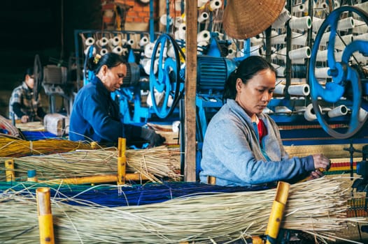 Vietnamese women Asian weavers works at a looms weaving machines in workshop at a factory for the production of woven reed mats in Asia. An Cu, Tuy An, Phu Yen province, Vietnam - April 14, 2025