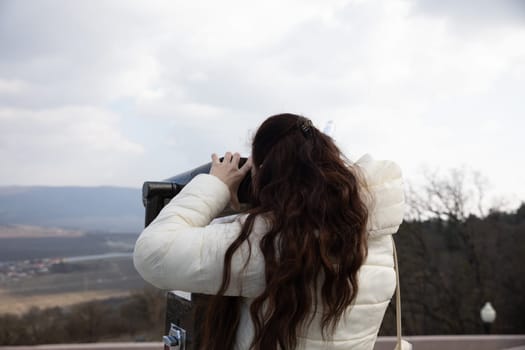 Woman looking through binoculars from the top of a mountain at the landscape