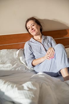 Brunette in pajamas woke up in the morning in the bedroom on the bed smiling