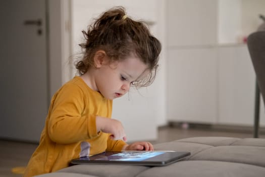 Little girl learning to draw digitally with a tablet in the living room. Playful and educational screen time for kids.