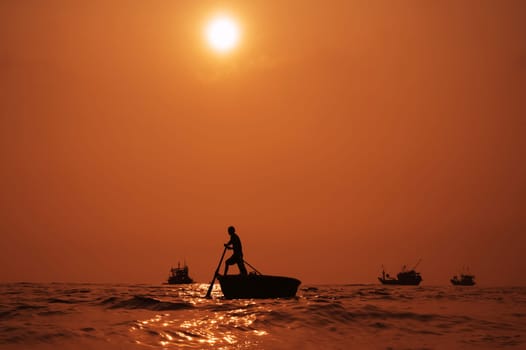 Silhouette of Vietnamese male fisherman on a round basket boat in the sea in a fishing village in the morning at sunrise in Vietnam
