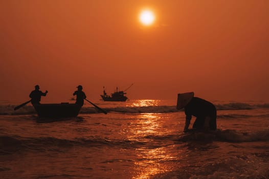 Silhouettes of Vietnamese fishermen in a round basket boat and a woman in a straw hat in fishing village in morning at sunrise in Vietnam