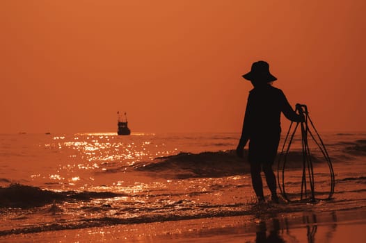 Silhouette of Vietnamese woman on the shore of sea with ship in a fishing village in morning at sunrise in Vietnam
