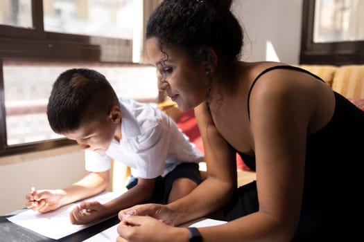 Mother carefully supervising her son drawing and learning, promoting education and family bonding