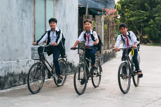 Happy Asian Vietnamese children school boys friends in school uniforms riding bicycles in the village. An Cu, Tuy An, Phu Yen province, Vietnam - April 14, 2025