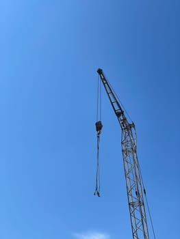 Metal construction crane at construction site with blue sky background