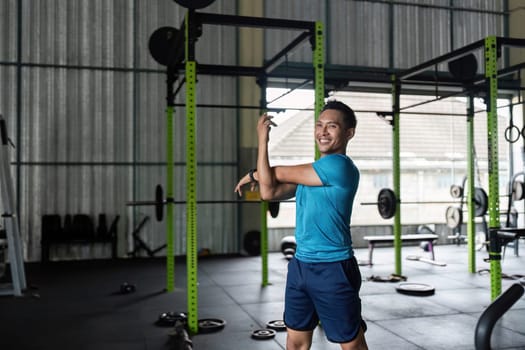 A cheerful male athlete stretches in a gym, showcasing positivity and motivation in fitness training.