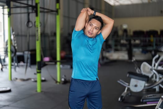 A focused man reaching his arm overhead to stretch in a gym, emphasizing fitness and flexibility. Highlights health and wellness.