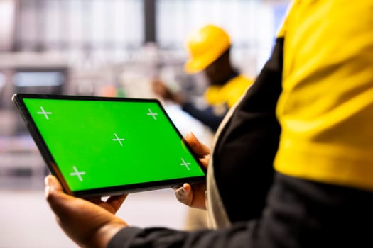Manufacturing engineer presenting a tablet with isolated copyspace in industrial workspace. Selective focus of device displaying blank chromakey screen held by smart factory employee.